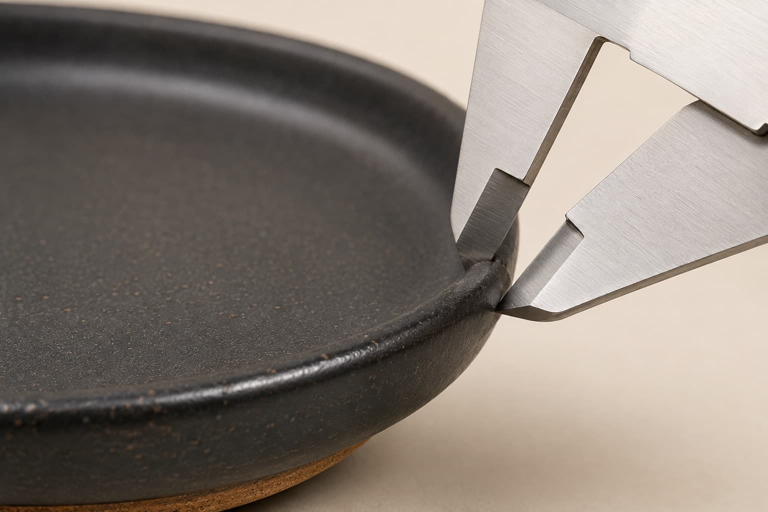 Vernier callipers closed onto the rolled rim of a charcoal stoneware plate.